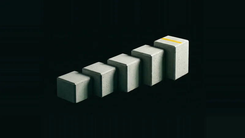 Five pale concrete test cubes stepped in ascending height on black, the tallest marked with a yellow stripe