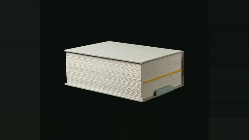 A thick closed specification book lit by low raking light in darkness, one yellow ribbon marker deep inside