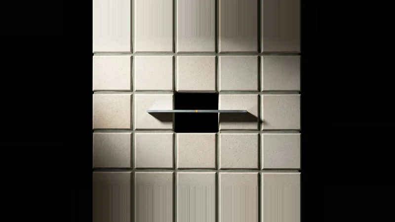 Overhead view of a pale concrete tile grid with one tile missing, a steel rule bridging the black gap