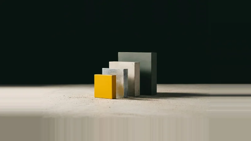 Low-angle photo of five metal gauge blocks in a row on concrete, the smallest one yellow, against black.