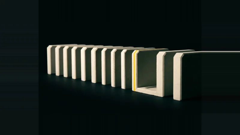 Low-angle view of twelve pale concrete blocks in a row, one slot empty, rim-lit against black.