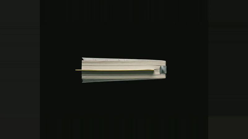Edge-on stack of pale specification pages in darkness, one inner sheet protruding with a yellow-lit edge.