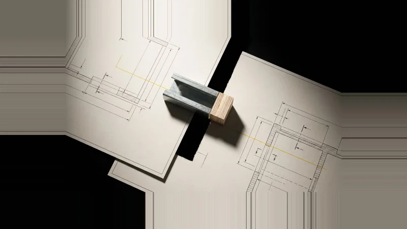 Overhead view of two off-white drawing sheets separated by a black gap, bridged by a metal frame offcut and wood block.