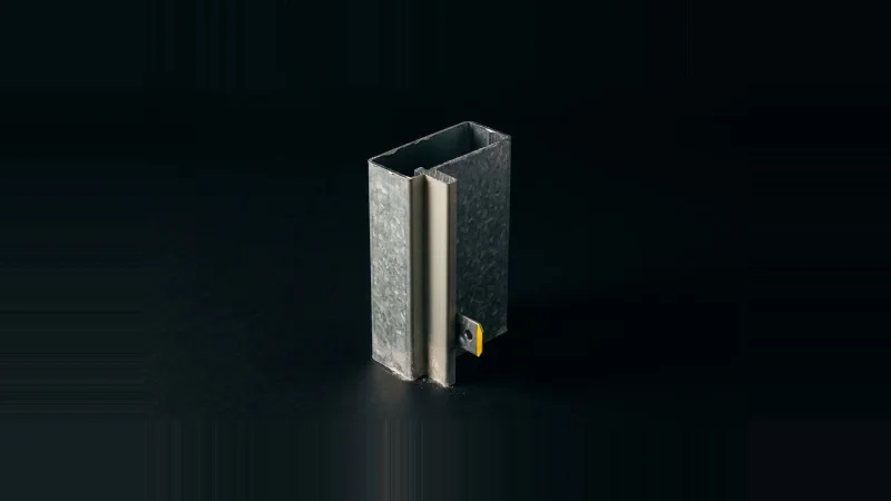 Cut section of a galvanised hollow metal door frame jamb standing upright in darkness, one anchor tab edged in yellow.