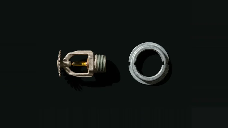 Overhead close-up of a pendent fire sprinkler head with its escutcheon ring detached, isolated on black