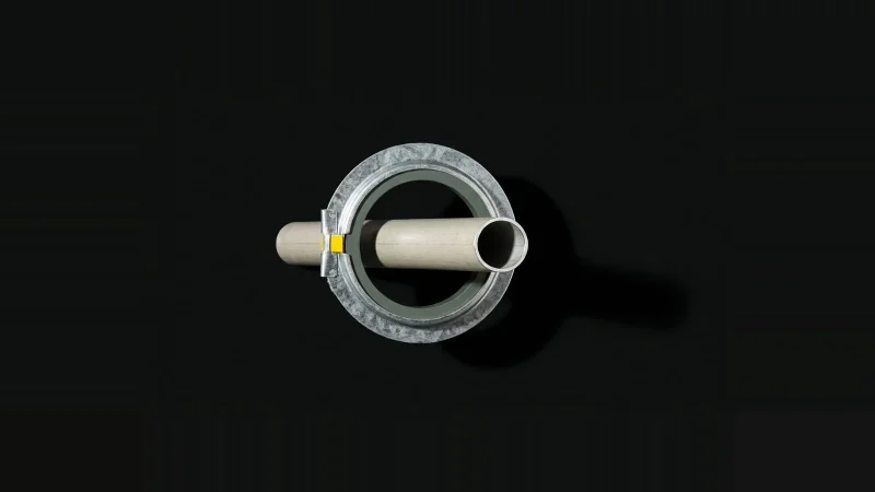 Overhead view of a galvanised intumescent firestop collar with a cut conduit stub, isolated on black