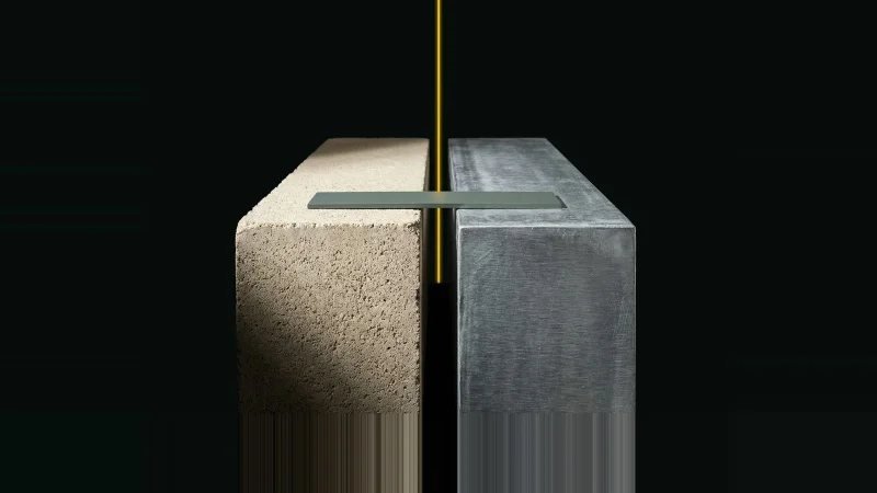 Two heavy concrete and metal blocks nearly touching, a narrow unfilled seam between them lit by a thin yellow line.