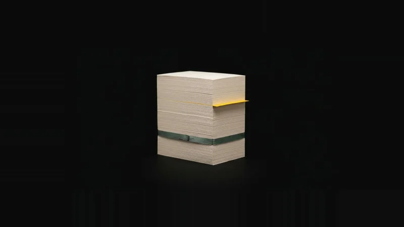 A tall block of stacked off-white paper standing upright in darkness, one sheet edged in yellow jutting out.
