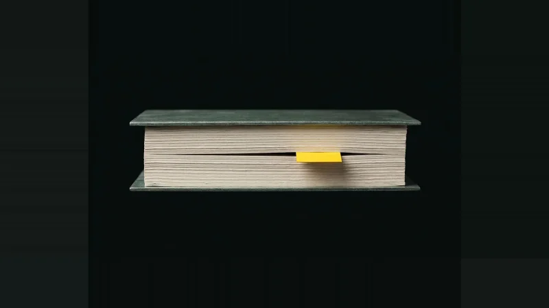 Edge-on stack of pale drawing sheets with one sheet missing, a yellow tab marking the gap, on black.