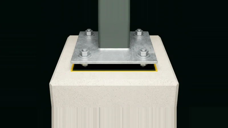 Galvanised steel base plate bolted above a concrete pier, an unfilled grout gap beneath marked by a yellow line.