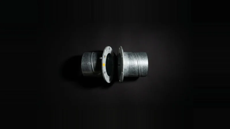 Two galvanised duct flanges laid end to end but misaligned, separated by a dark gap, lit from one side