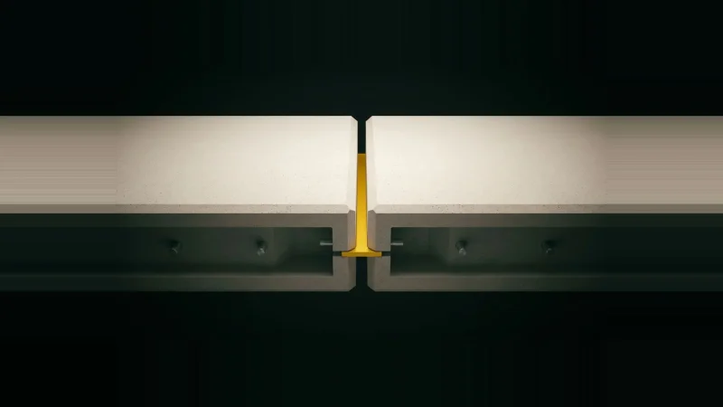 Two pale concrete blocks with a misaligned gap between them, bridged by a single machined yellow shim, on black.