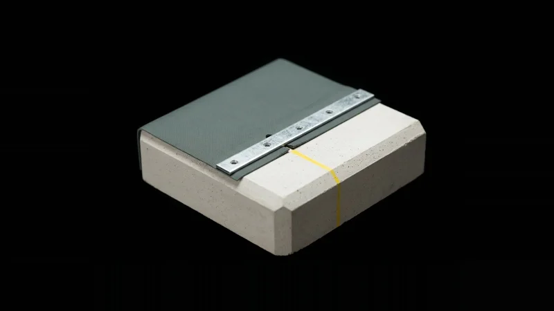 Close-up of a concrete and membrane termination detail with a galvanised bar, a small unsealed gap and a yellow chalk line.