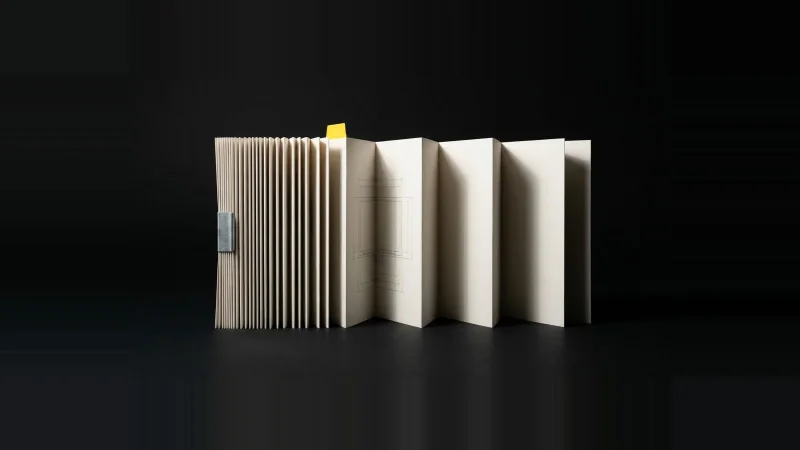A folded strip of pale specification paper, tightly pleated at one end and open at the other, with a small yellow tab.
