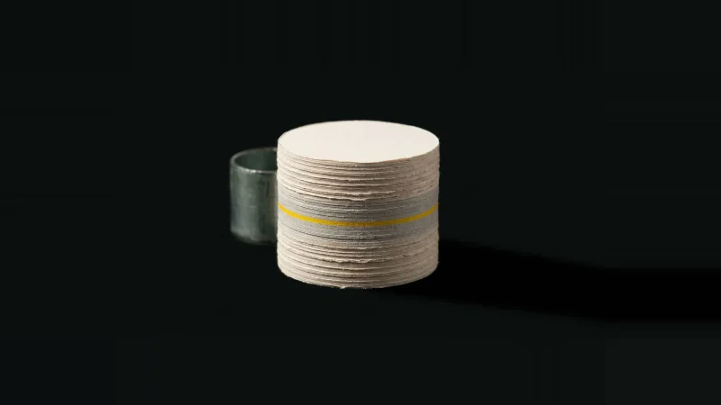 A paper core sample drilled from a spec book stands on end in darkness, one thin layer glowing yellow.