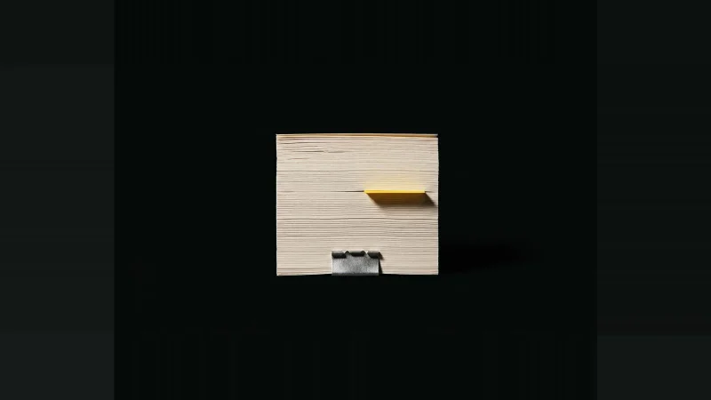 A small block of off-white paper clipped in brushed steel, one yellow index tab protruding, isolated on black.