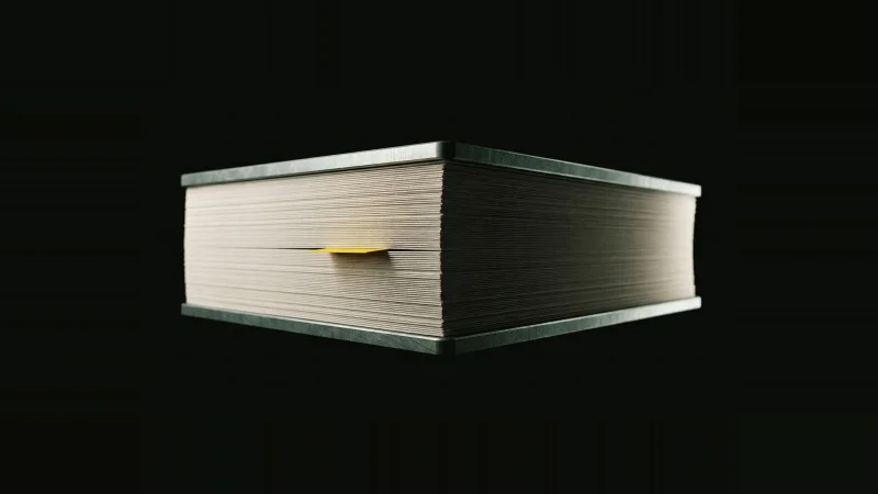 Edge-on stack of off-white paper clamped between metal plates on black, one yellow index tab lit