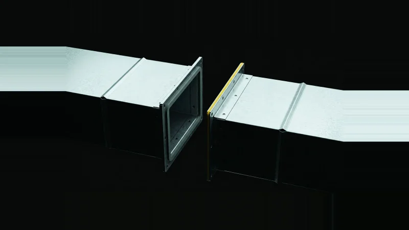 Two galvanised duct sections rim-lit in darkness, their bolt flanges stopping short of each other with a gap between