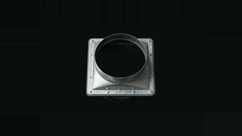 Overhead close-up of a galvanised duct transition fitting, its bolted flange seam broken by a thin yellow-lit gap.