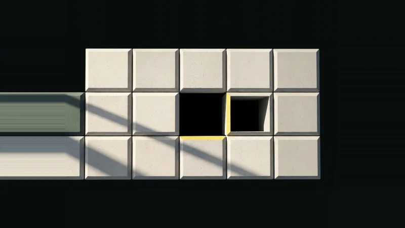 Overhead view of a grid of pale concrete tiles with one square missing, a yellow line marking the empty gap.