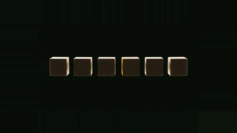 A straight row of small pale concrete cubes in darkness, one cube missing, the gap's edge lit by a thin yellow line.