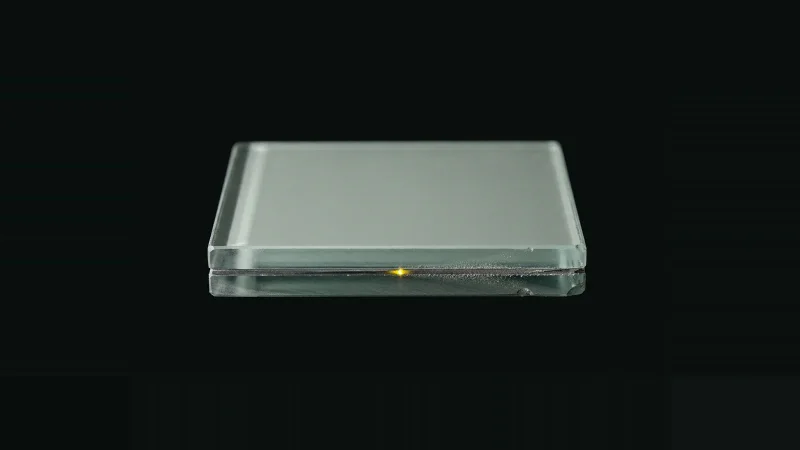 Close-up of a cut edge of lead-lined glass on black, revealing a thin lead layer inside the laminate.
