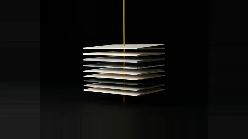 Exploded stack of pale paper and metal layers pierced by a thin yellow rod, one layer misaligned, on black