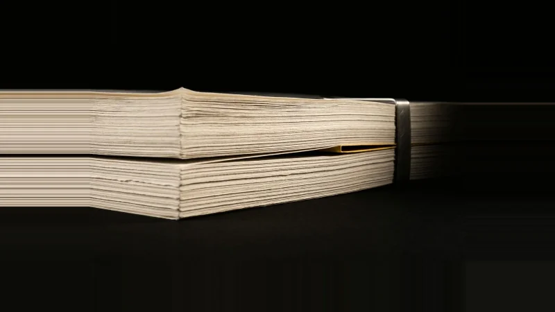 Low-angle close-up of a stack of off-white document sheets with one sheet missing, yellow light in the gap