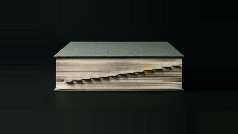 A thick specification book seen edge-on, a metal index tab on every page, one tab bright yellow.