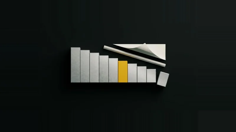 Overhead view of stepped steel gauge blocks in a calibrated row, one yellow, one skewed out of line, on black.